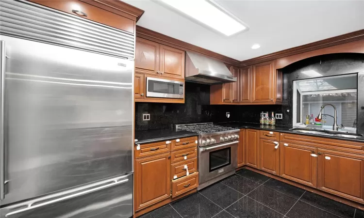 Kitchen with backsplash, range hood, sink, premium appliances, and dark stone counters