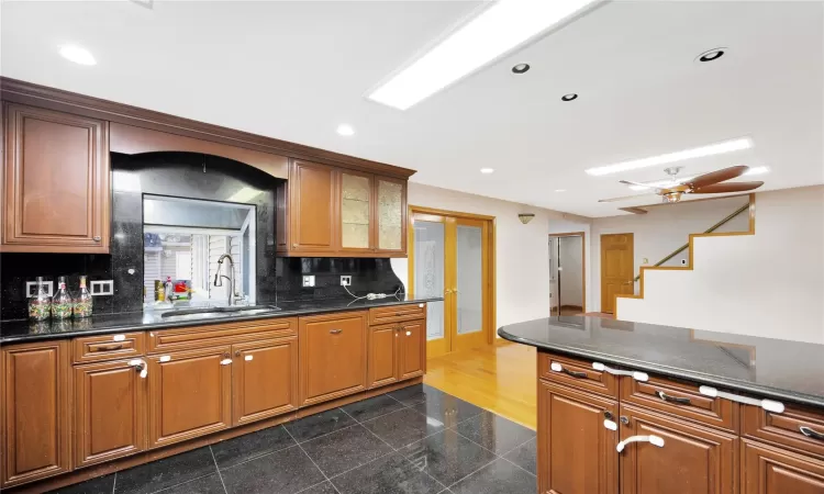 Kitchen featuring ceiling fan, sink, dark stone counters, and tasteful backsplash