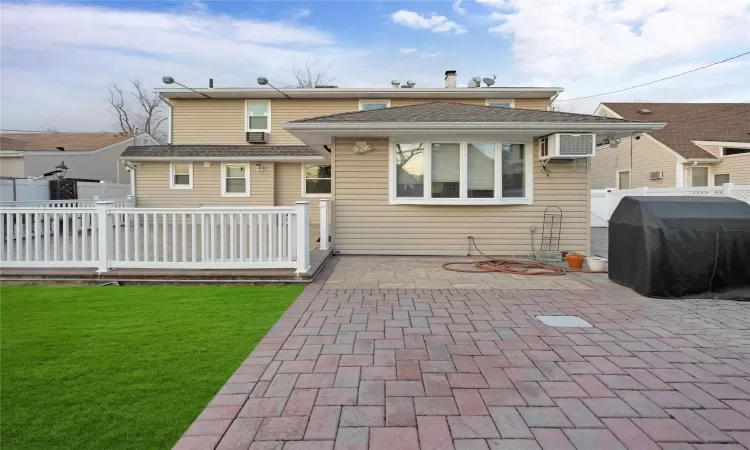 Back of property with a wall mounted air conditioner, a yard, and a patio