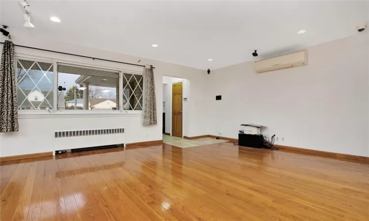 Empty room with radiator, wood-type flooring, and a wall mounted air conditioner