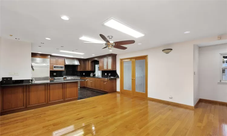 Kitchen with wall chimney exhaust hood, french doors, built in appliances, kitchen peninsula, and hardwood / wood-style flooring