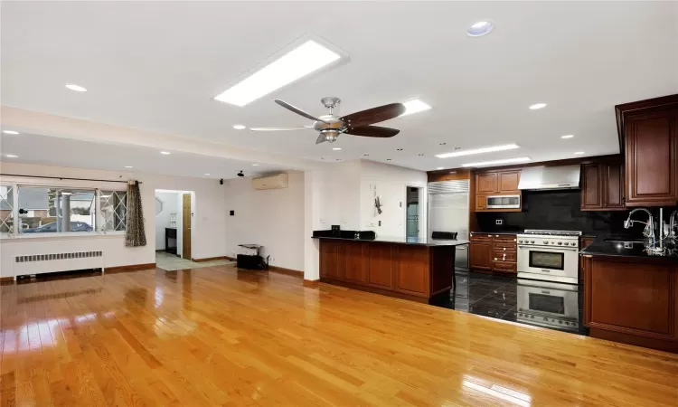 Kitchen with radiator heating unit, wood-type flooring, built in appliances, tasteful backsplash, and sink