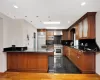 Kitchen featuring kitchen peninsula, dark wood-type flooring, wall chimney range hood, built in appliances, and sink