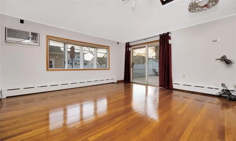 Unfurnished room featuring crown molding, hardwood / wood-style floors, an AC wall unit, and a baseboard radiator