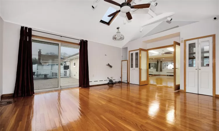 Spare room featuring ceiling fan, vaulted ceiling with skylight, hardwood / wood-style floors, and a baseboard heating unit