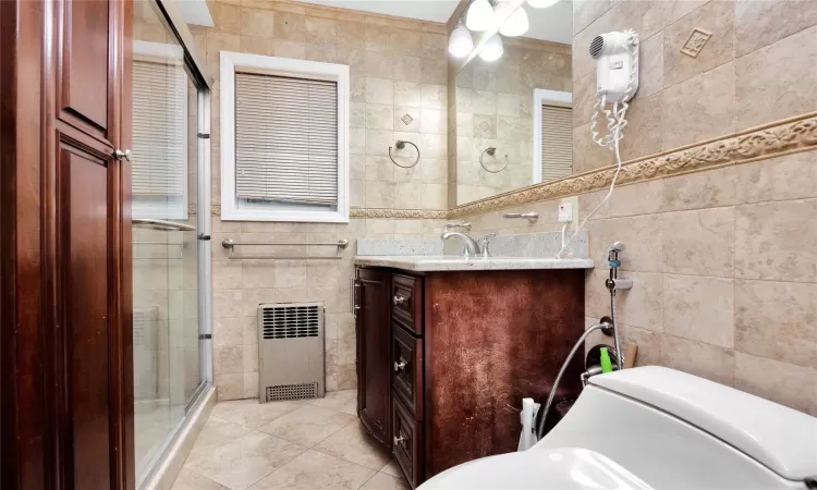 Bathroom with a shower with door, tile walls, tile patterned floors, and vanity