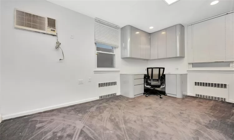 Unfurnished office with radiator, carpet floors, and an AC wall unit