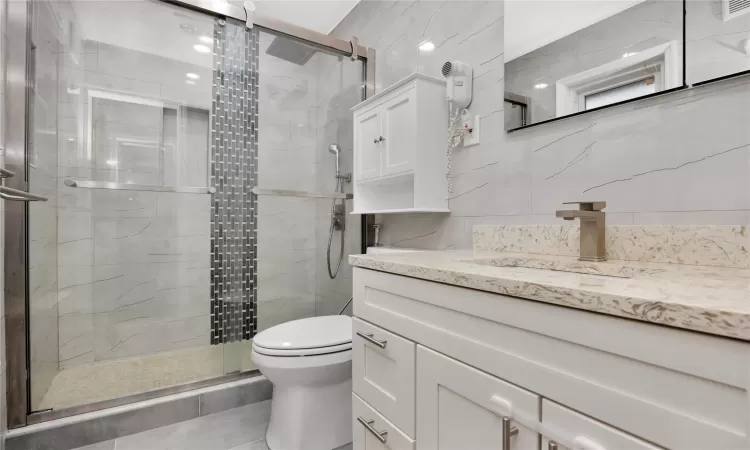 Bathroom featuring toilet, a shower with door, and vanity