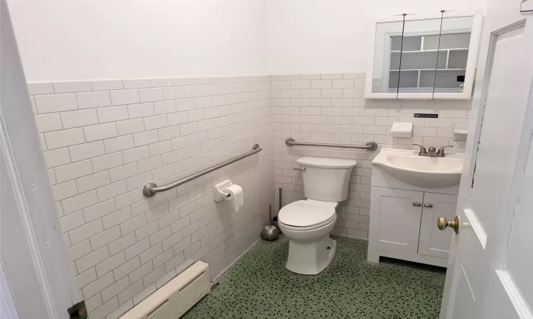 Bathroom with toilet, vanity, tile walls, and a baseboard radiator