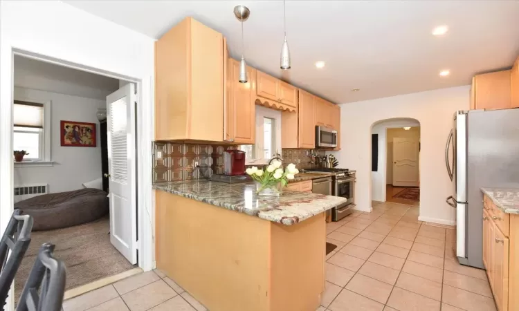 Kitchen with tasteful backsplash, kitchen peninsula, hanging light fixtures, light brown cabinets, and stainless steel appliances