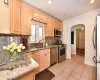 Kitchen with stainless steel appliances, light brown cabinetry, sink, decorative backsplash, and light tile patterned floors