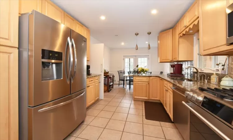 Kitchen with stainless steel appliances, light brown cabinetry, dark stone countertops, and kitchen peninsula