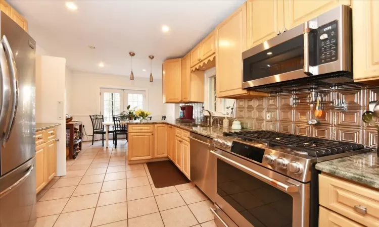 Kitchen featuring light brown cabinetry, sink, appliances with stainless steel finishes, and dark stone countertops