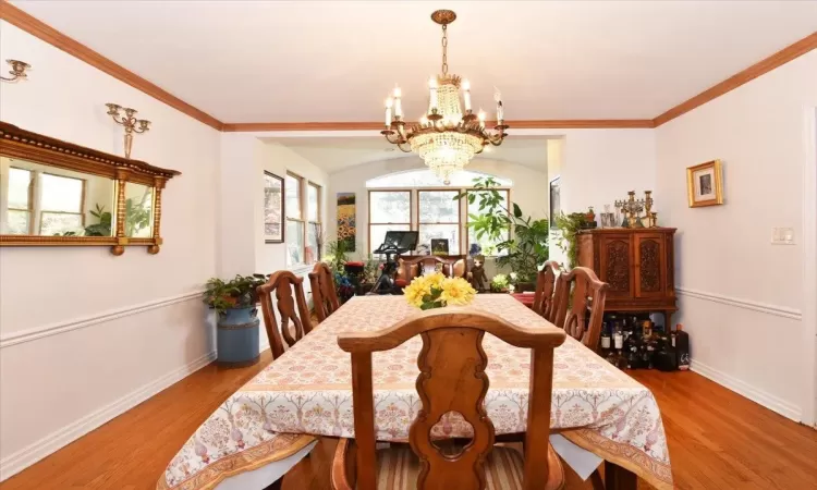 Dining area with light hardwood / wood-style floors, ornamental molding, and a notable chandelier