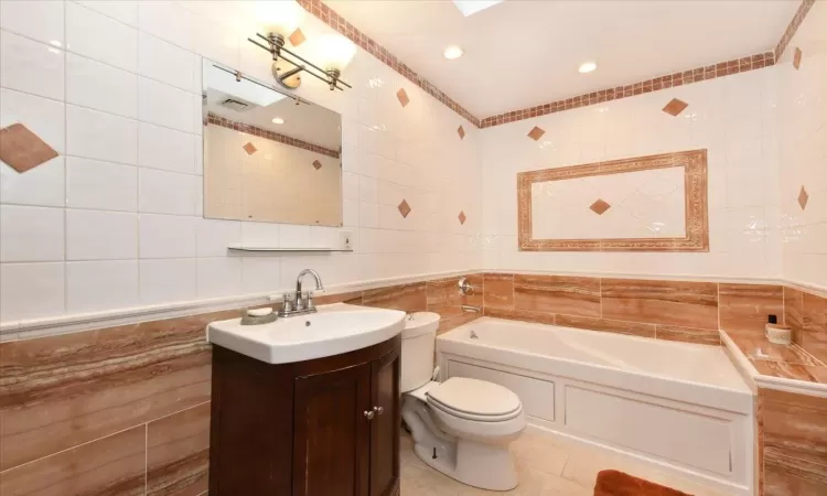 Bathroom with tile patterned floors, vanity, tile walls, toilet, and a bath