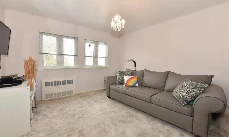 Living room featuring light colored carpet, radiator, and a chandelier