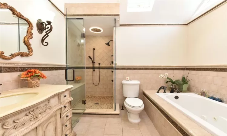 Full bathroom featuring toilet, vanity, tile patterned flooring, tile walls, and plus walk in shower