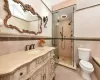 Bathroom featuring toilet, vanity, tile walls, tile patterned floors, and a shower with door