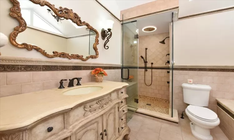 Bathroom featuring toilet, vanity, tile walls, tile patterned floors, and a shower with door