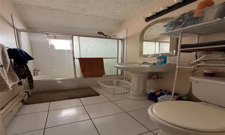 Bathroom with toilet, tiled shower / bath, a baseboard heating unit, tile patterned floors, and a textured ceiling