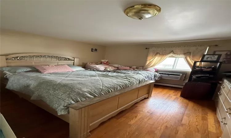 Bedroom featuring light hardwood / wood-style flooring, baseboard heating, and a wall mounted air conditioner