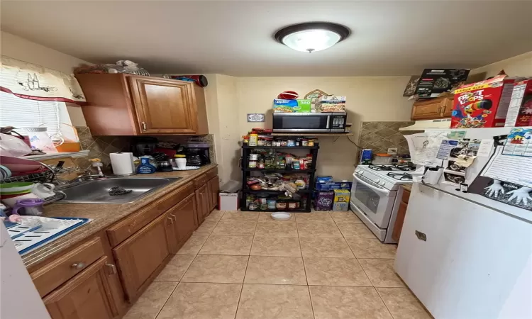 Kitchen featuring sink, white appliances, light tile patterned floors, and tasteful backsplash