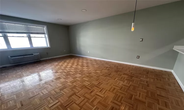 Empty room with an AC wall unit and parquet floors