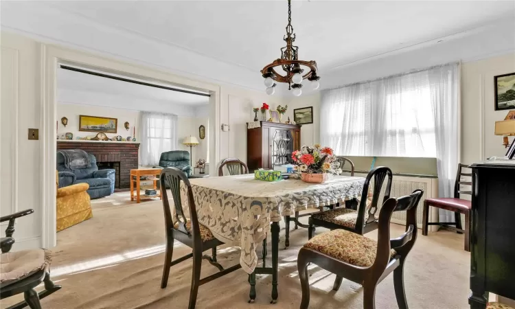 Carpeted dining area with a brick fireplace, a wealth of natural light, and a notable chandelier