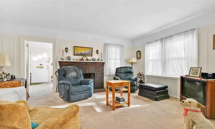 Living room featuring light carpet, a fireplace, and radiator heating unit