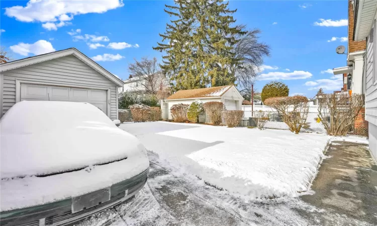 Yard layered in snow featuring a garage and an outdoor structure