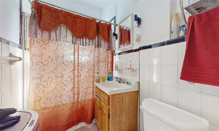 Bathroom featuring toilet, tile walls, and vanity