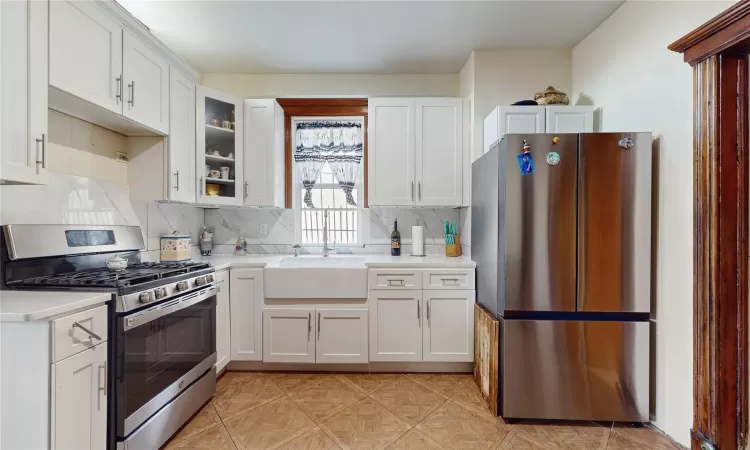 Kitchen with stainless steel appliances, decorative backsplash, white cabinetry, and sink