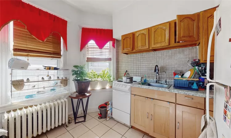 Kitchen with white appliances, radiator heating unit, sink, backsplash, and light tile patterned flooring