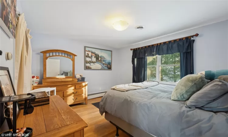 Bedroom with light hardwood / wood-style flooring and a baseboard heating unit