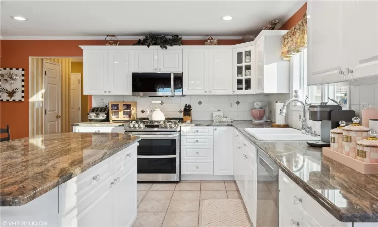 Kitchen featuring sink, backsplash, white cabinetry, light tile patterned floors, and stainless steel appliances