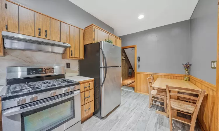 Kitchen with a baseboard radiator, appliances with stainless steel finishes, light hardwood / wood-style flooring, and exhaust hood