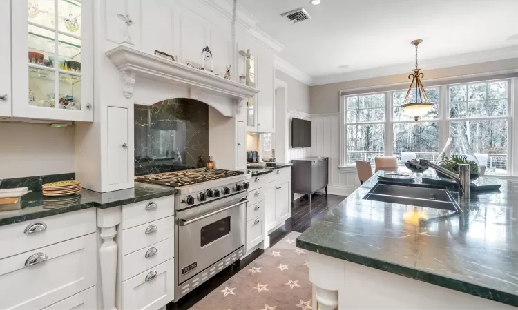 Kitchen featuring premium stove, decorative light fixtures, sink, and white cabinetry