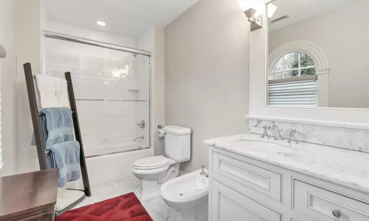 Full bathroom with bath / shower combo with glass door, toilet, vanity, and a bidet