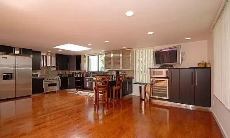 Kitchen featuring wine cooler, wall chimney range hood, decorative backsplash, wood-type flooring, and premium appliances