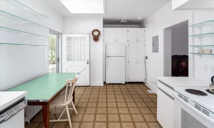 Kitchen featuring electric panel, a skylight, white cabinets, and white appliances