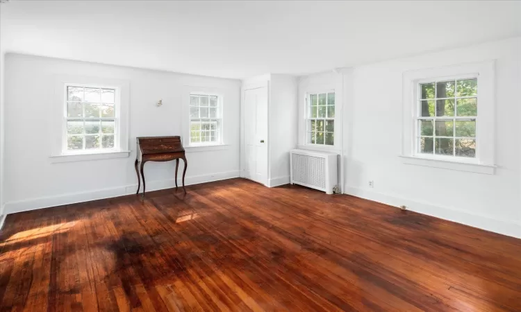 Empty room featuring dark wood-type flooring and radiator heating unit