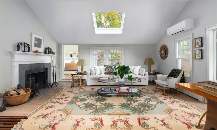 Living room with a healthy amount of sunlight, a wall mounted AC, lofted ceiling with skylight, and wood-type flooring