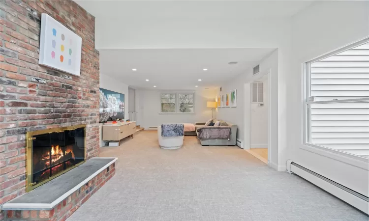 Carpeted living room featuring a brick fireplace and a baseboard radiator