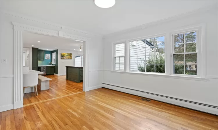 Unfurnished living room with baseboard heating, wood-type flooring, and crown molding