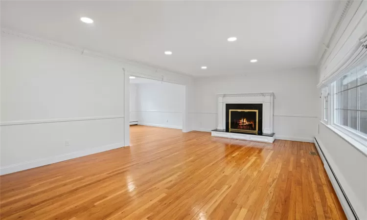 Unfurnished living room featuring light wood-type flooring, baseboard heating, crown molding, and a fireplace