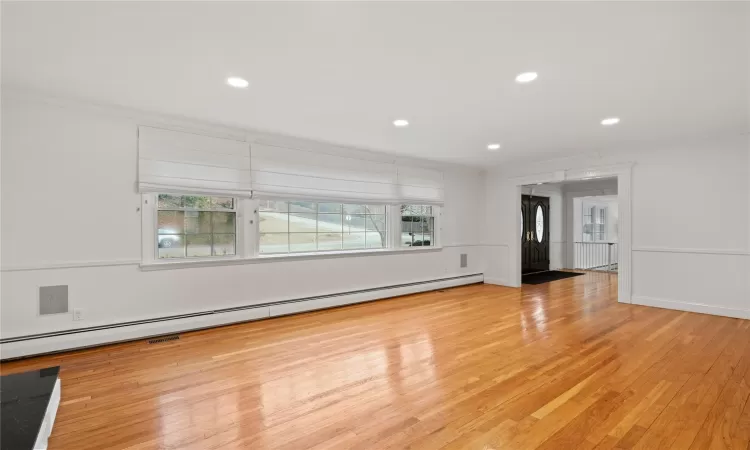 Unfurnished living room with baseboard heating, crown molding, and light wood-type flooring