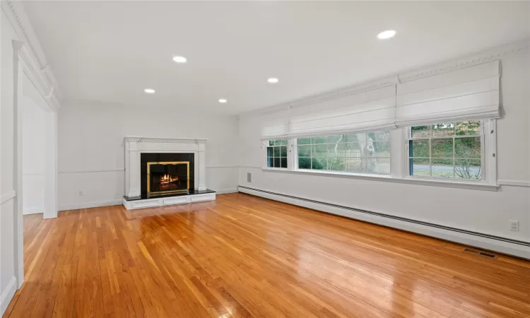 Unfurnished living room featuring a baseboard heating unit, a wealth of natural light, ornamental molding, and light hardwood / wood-style flooring