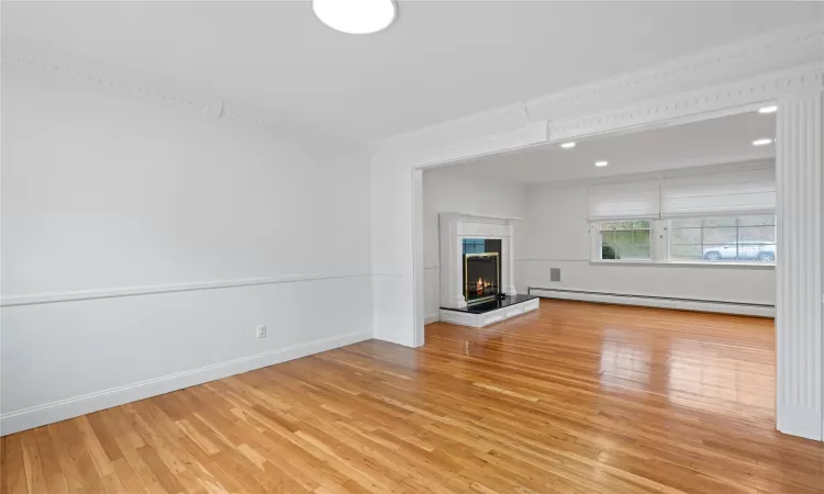 Unfurnished living room featuring a baseboard heating unit, ornamental molding, and light hardwood / wood-style floors