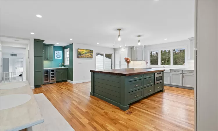 Kitchen featuring stainless steel microwave, light hardwood / wood-style floors, butcher block countertops, hanging light fixtures, and green cabinetry