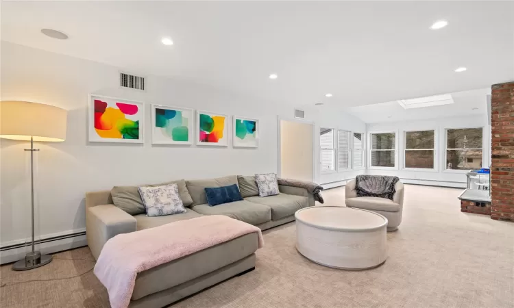 Living room featuring baseboard heating, light colored carpet, and lofted ceiling with skylight